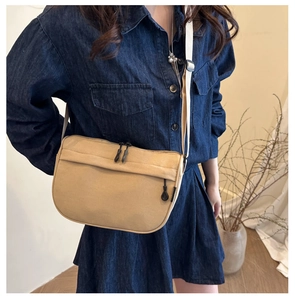 Close-up of khaki canvas shoulder bag with black zippers and adjustable white strap