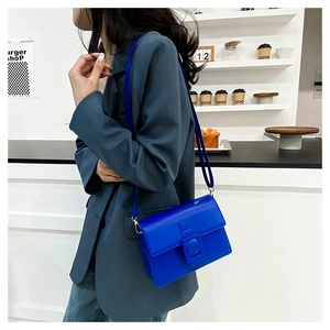 Detail of royal blue crossbody bag with oversized buckle on a lifestyle cafe background