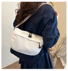 Detail of white crescent canvas crossbody bag with black zippers on blue denim outfit