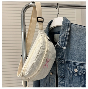 Détail du sac banane croissant crème avec broderie de nœud rose et texture en nylon plissé