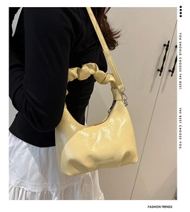 Detail of light yellow patent leather handbag with a stylish scrunchie handle and logo