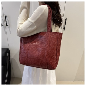 Detail of burgundy woven texture tote bag worn on shoulder in minimalist setting