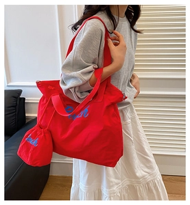 Detail of red canvas tote bag featuring blue Peach embroidery and matching drawstring pouch