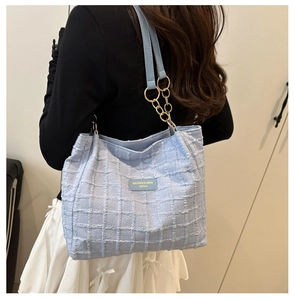 Detail of light blue textured tote bag with metal chain strap worn on the shoulder