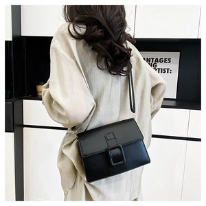 Detail of minimalist black leather crossbody bag with belt buckle on light outfit