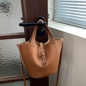 Brown litchi grain leather bucket bag with metal buckle hanging on a wooden door handle