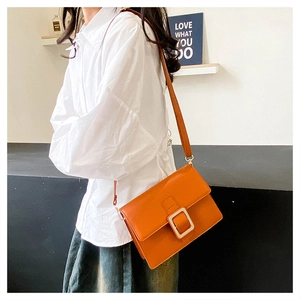 Detail of orange crossbody bag with a large silver buckle and adjustable shoulder strap