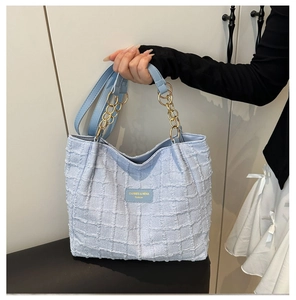 Detail of light blue tweed tote bag with golden chain handle and woven texture