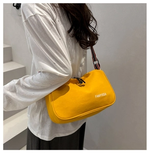 Détail du sac bandoulière en toile jaune avec sangle rayée porté par un mannequin