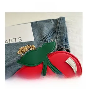 Close-up of red cherry bag featuring green leaf details and a golden metal chain strap