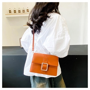 Detail of orange leather crossbody bag featuring a large silver square metal buckle