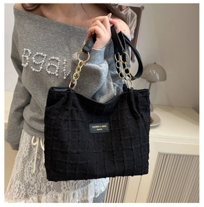 Detail of waffle-textured black tote bag with gold chain strap and brand emblem