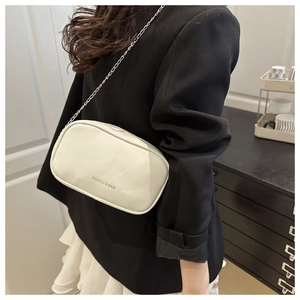 Detail view of a white PU leather pillow bag with silver chain strap and logo lettering