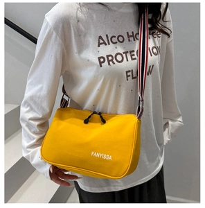 Détail d'un sac bandoulière en toile jaune vif avec sangle rayée et logo imprimé