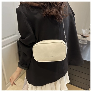Detailed view of cream-colored square crossbody bag with gold chain strap on model