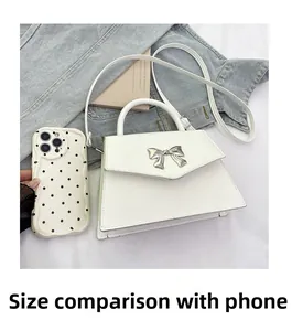 Mini white handbag with silver bow detail shown next to a phone for size comparison