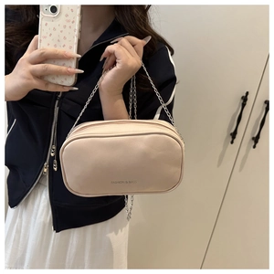 Detail of a minimalist cream leather crossbody bag with silver chain strap worn by a model