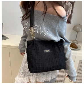 Detail of black quilted large shoulder bag with gold chain strap and square label
