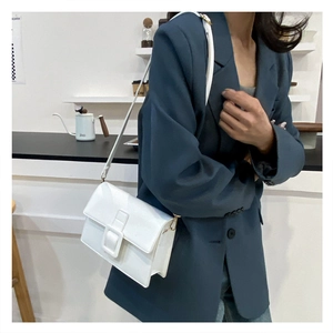 Detail of white rectangular crossbody bag with decorative buckle on navy blazer