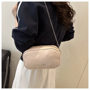 Détail du sac carré minimaliste en cuir blanc cassé avec logo et bandoulière chaîne