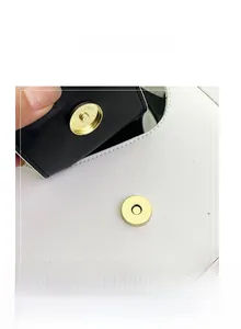 Dettaglio ravvicinato della chiusura magnetica dorata sulla borsa in pelle bianca
