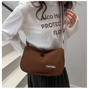 Sac bandoulière en nylon marron avec sangle rayée porté sur un t-shirt blanc