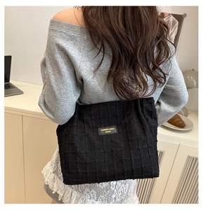 Close-up of black textured checkered tote bag with gold chain strap on shoulder