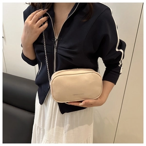 Détail d'un sac bandoulière beige avec chaîne argentée et lettrage décoratif mode