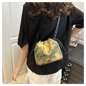 Detail of landscape print drawstring bucket bag worn as a crossbody shoulder bag