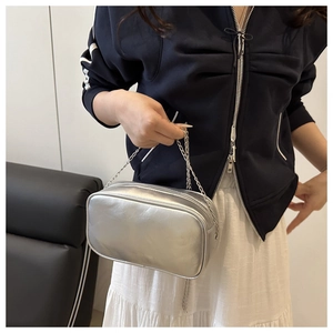 Detail showing a silver metallic Boston bag with a chain strap held by a model