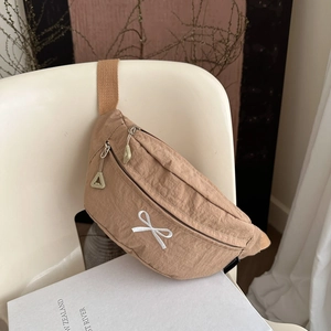 Sac de poitrine en nylon kaki avec broderie nœud blanc sur une chaise minimaliste