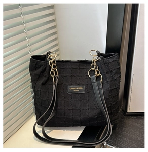 Detail of black quilted tote bag with gold chain strap and branding on textured fabric
