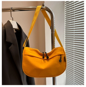 Detail of a bright yellow crescent canvas bag with dual zippers on a metal hanger