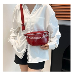 Detail of glossy red patent leather saddle bag with silver chain and wide strap