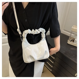 Detailed view of white pleated handbag featuring cloud handle and adjustable strap worn by model
