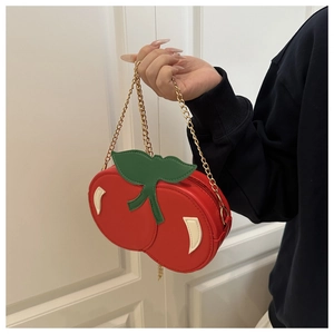 Detail view of a creative cherry shaped crossbody bag with gold chain and green leaf deco