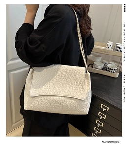 Détail du sac à bandoulière beige tressé avec chaîne dorée porté par un mannequin