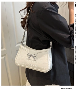 Detail of white crocodile embossed texture on shoulder bag with silver bow buckle