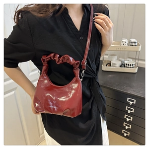 Deep red pleated crescent shoulder bag with glossy patent finish and chain strap details