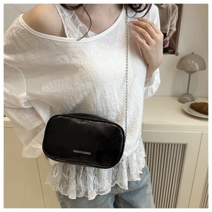 Détail d'un petit sac bandoulière en cuir PU brillant noir avec chaîne et logo blanc