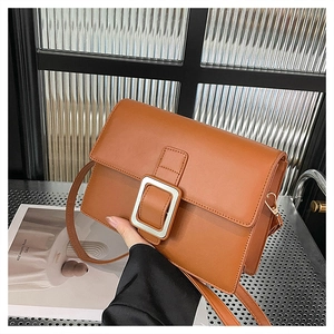 Detail of brown leather crossbody bag with white square buckle and gold metal hardware