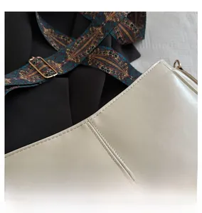 Detail of minimalist cream leather handbag featuring vertical stitching and colorful strap