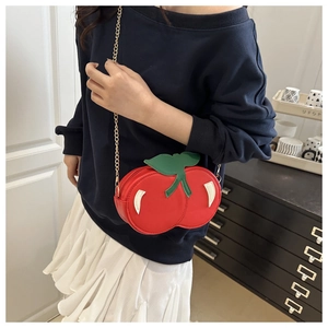 Detailed view of creative cherry-shaped crossbody bag with gold chain on model