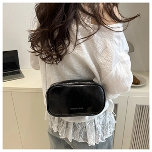Close-up of stylish black glossy leather crossbody bag with metal chain strap worn by model