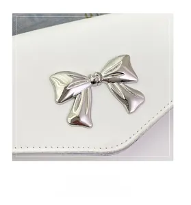 Detailed view of white leather crossbody bag with silver bow ornament and fine stitching