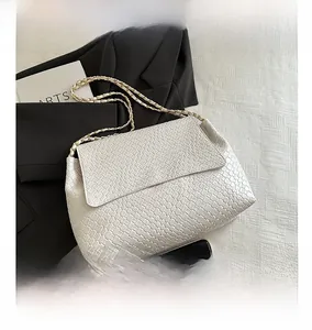 Détail d'un sac bandoulière blanc texturé avec chaîne en métal à côté d'un smartphone