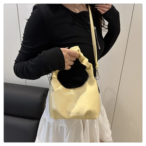 Detail of light yellow patent leather bucket bag with pleated handle and fashion text