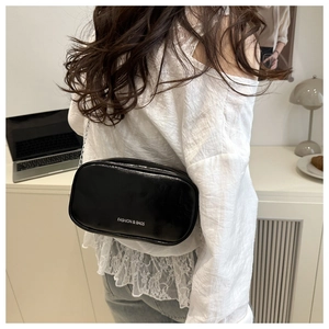 Detail of black glossy chain bag with white fashion text shown on a model's shoulder
