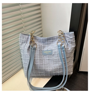 Detail of light blue textured tweed tote bag with gold chain strap and brand patch