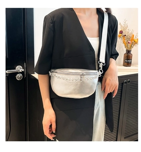Metallic silver saddle bag with wide canvas strap and chain detail on a black blazer
